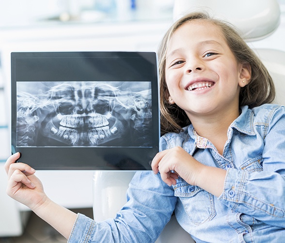 Young girl holding up x-rays during her first dental office visit